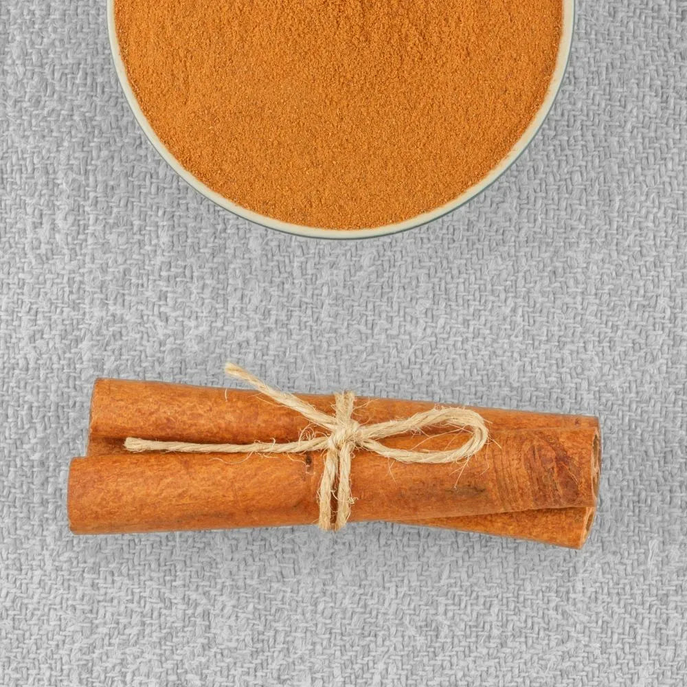 Cannelle en tuyaux entourée d’une ficelle et posée à côté d’un pot de cannelle en poudre