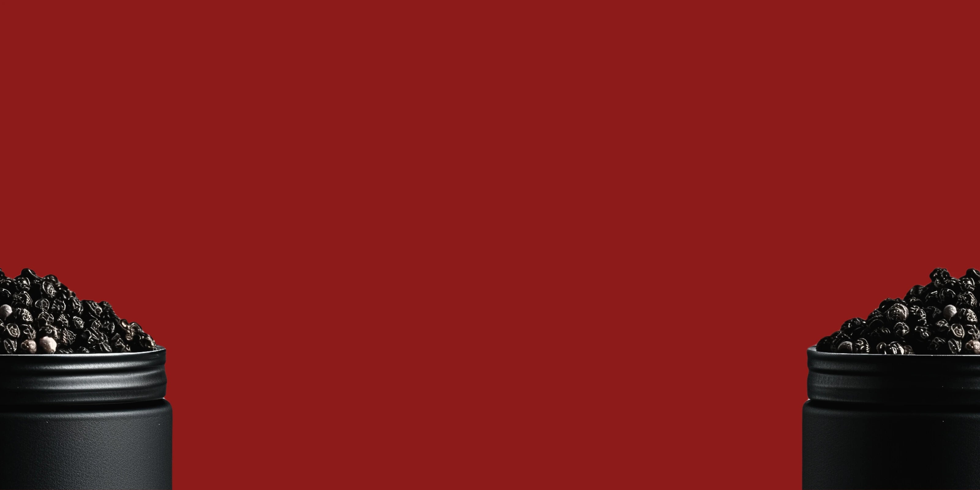 Image de grains de poivre de Madagascar dans un pot noir en métal coupé en deux avec un fond rouge