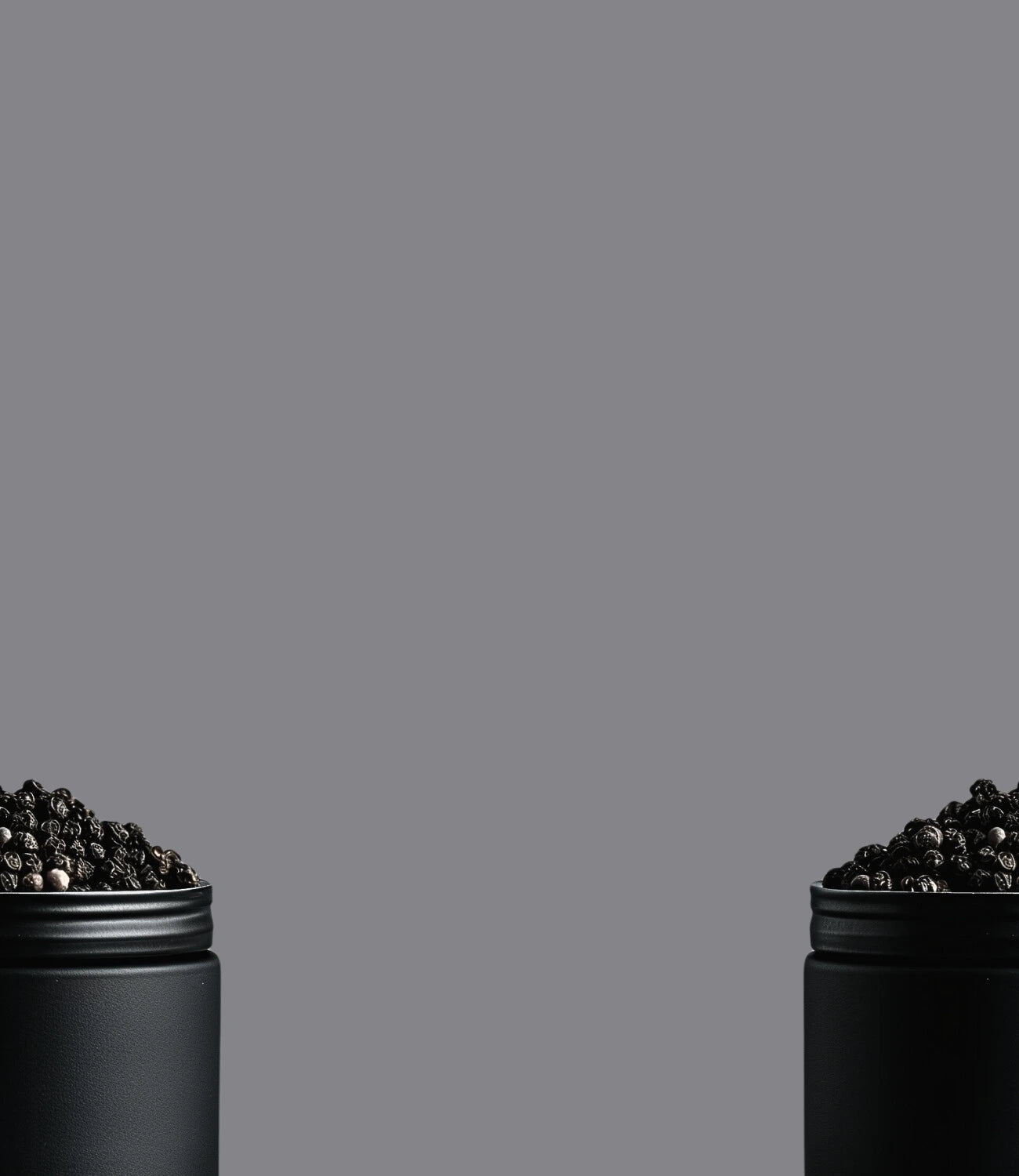 Image de grains de poivre de Madagascar dans un pot noir en métal coupé en deux avec un fond gris