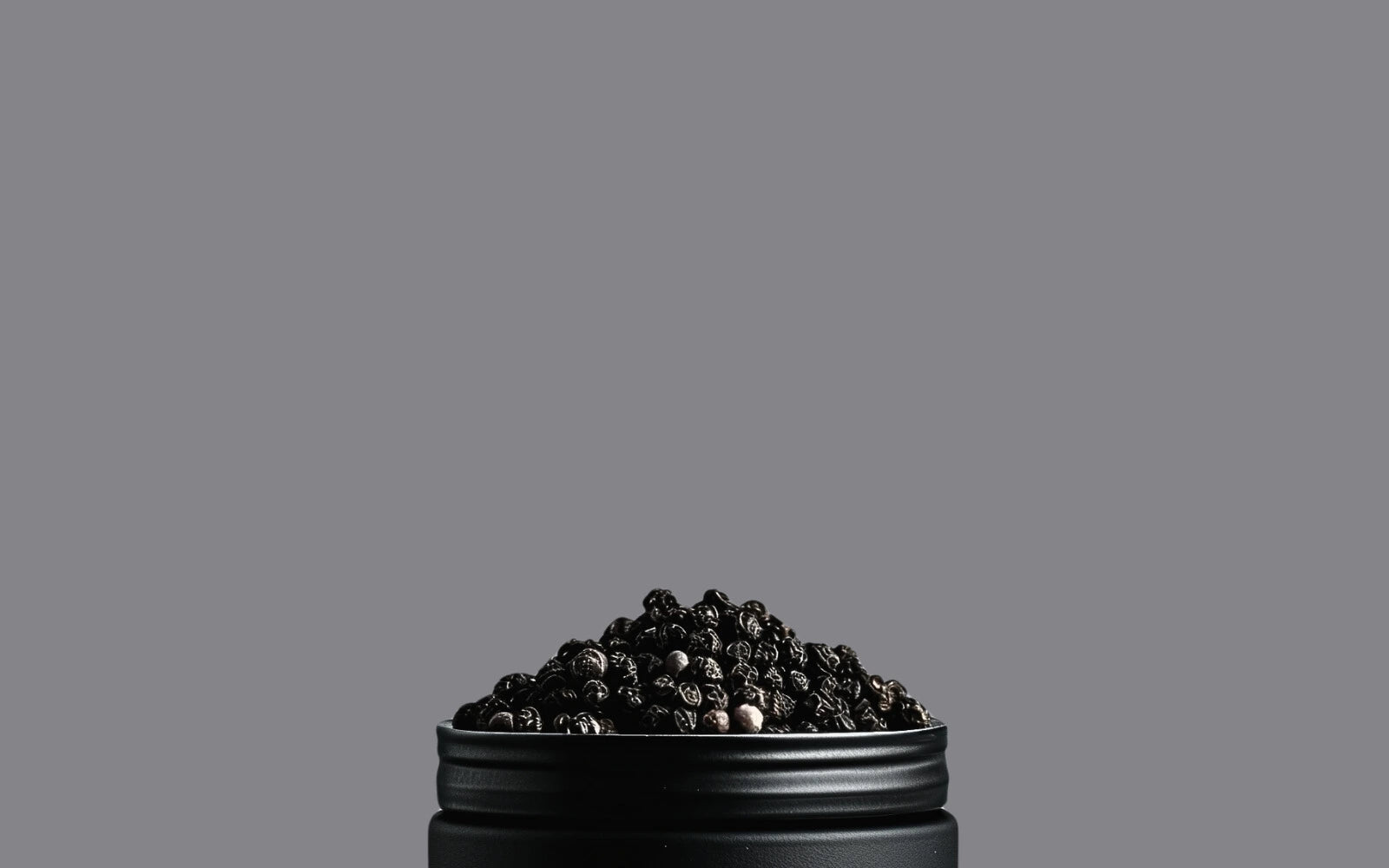 Image de grains de poivre de Madagascar dans un pot noir avec un fond gris